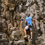 Man rock climbing while wearing our Lazy Dog Original Oval Logo Polyblend t-shirt in heather blue color with white and black screen printing of border collie lounging . Shirt reads, "Lazy Dog Key West."
